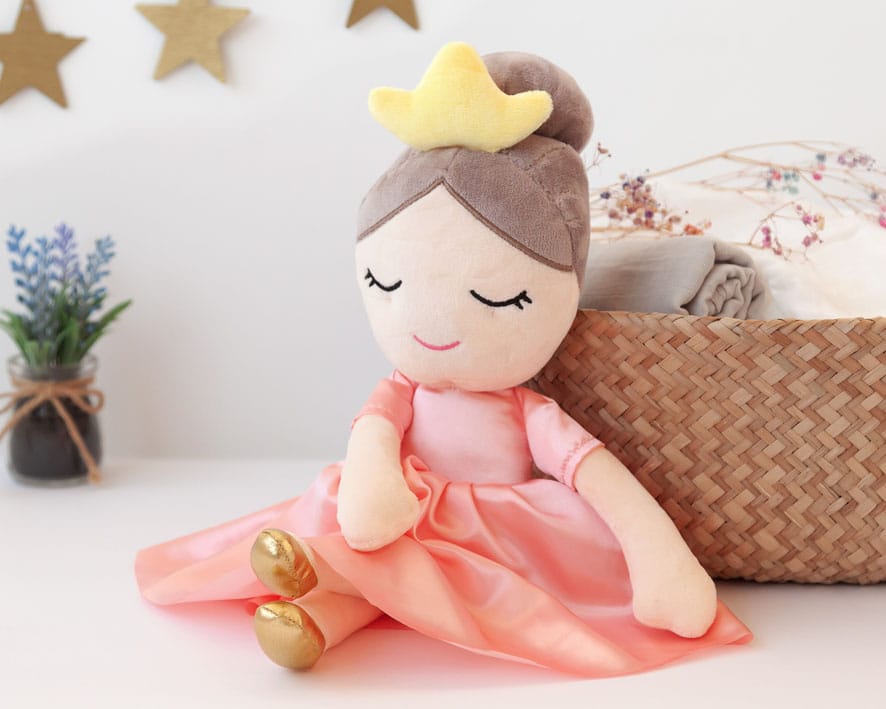 Peluche de muñeca Princesa con corona dorada y vestido rosa, junto a una cesta de regalo