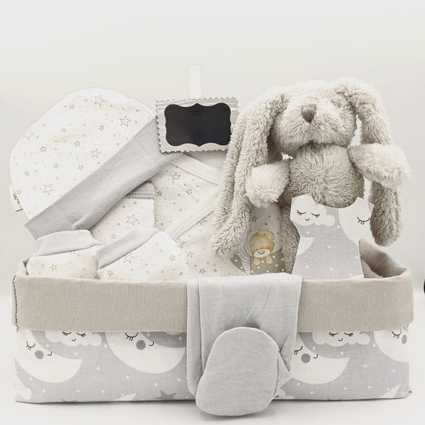 Canastilla de bebé Luna con conejito de peluche gris, ropa blanca con estrellas y caja de tela gris con lunas