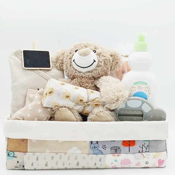 Canastilla Osito Teddy con oso de peluche, muselina, ropa beige y productos de higiene en caja de tela patchwork